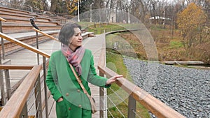 Autumn caucasian woman stands in large wooden park area Railing is leant over