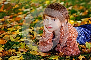 Autumn children. A boy in an autumn Park lies on the grass among yellow maple leaves. A child walks in the Park