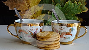 Autumn collage. On white, two painted Chinese tea cups with a drink, cookies. In the background is a blk background with autumn .