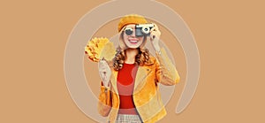 Autumn color style outfit, beautiful young woman photographer with film camera holds yellow maple leaves wearing orange french