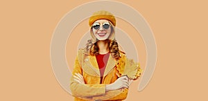 Autumn color style outfit, portrait of beautiful smiling young woman with yellow maple leaves wearing orange french beret hat,