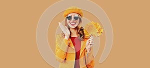 Autumn color style outfit, portrait of beautiful smiling young woman with yellow maple leaves wearing orange french beret hat,