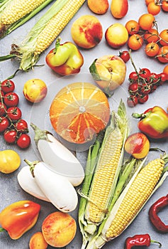 Autumn colorful vegetables and fruits set: apricots, tomatoes, paprika, pumpkin, corn, etc. on gray background, top view