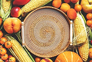 Autumn colorful vegetables and fruits set: apricots, tomatoes, pumpkin, paprika, corn, etc. and empty wicker tray on rustic wooden