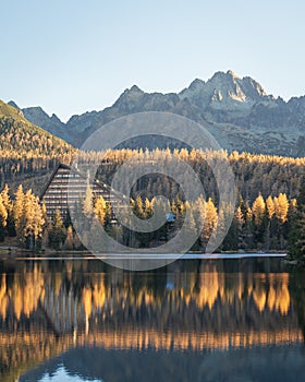 Podzimní barevná krajina s hotelem na břehu jezera se skalnatými horami v pozadí