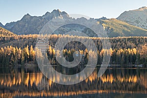 Autumn coloured landscape with a hotel on a bank of a lake with rocky mountains in background