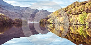 Autumn colours in Highlands of Scotland - trees, mountains, sky, hills, stones reflected in loch waters