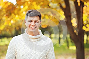 Autumn is coming! Be happy today! Close up portrait of young handsome brunette man staying in autumn park smiling