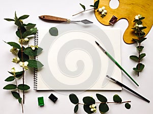 Autumn composition with album, watercolors and brushes, decorated with green snowberry branches and berries. Flat lay, top view