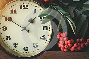 Autumn composition with a clock, cluster of mountain ash and yellow leaves against the clock