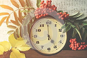 Autumn composition with a clock, cluster of mountain ash and yellow leaves against the clock