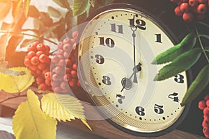 Autumn composition with a clock, cluster of mountain ash and yellow leaves against the clock