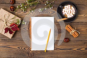 Autumn composition. Coffee with marshmallow, gift wrapped in kraft paper ,blank notepad, pencil, leaves cinnamon sticks and chestn