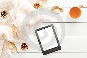 Autumn composition. Feminine desk table with knitted scarf, tea cup, cones, tablet ebook with blank screen, fall leaves on wooden