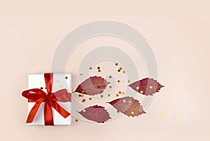 Autumn composition with gift box, dried leaves and golden confetti on pastel pink backgound.