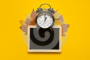 Autumn composition mockup banner with frame, dried leaves and black alarm clock on yellow background. Autumn, fall mock