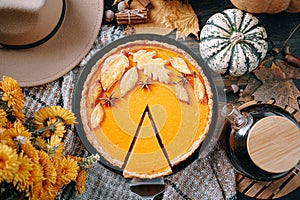 Autumn composition with pumpkins, yellow tea flowers, warm plaid and hat and pumpkin pie in the center of the frame