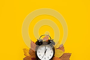 Autumn composition sale banner with dried leaves and black alarm clock on pastel yellow background. Autumn, fall Flat