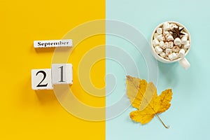 Autumn composition. Wooden calendar September 21, cup of cocoa with marshmallows and yellow autumn leaves on yellow blue