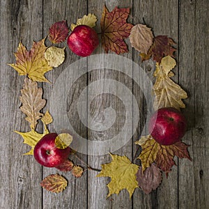 Autumn composition. Wreath made of autumn leaves and red apples on old wooden background. Flat lay, top view, copy space