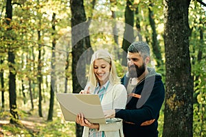 Autumn couple using notebook. Autumn outdoor portrait of beautiful happy girl and bearded man walking in park or forest