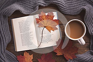 Autumn, cozy composition. Warm scarf, book, cup of coffee, maple leaves, on wooden background