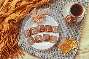 Autumn cozy flat lay. Top view. Hot tea cup and round white plate with cookies text HELLO FALL, orange warm scarf and autumn leav