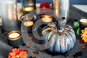 Autumn cozy mood composition for home decoration. Gray pumpkin with sequins, burning candles and fresh dahlia flowers on