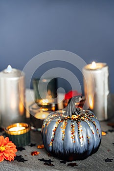 Autumn cozy mood composition for home decoration. Gray pumpkin with sequins, burning candles, fresh dahlia flowers on