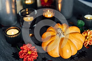 Autumn cozy mood composition for home decoration. Orange pumpkin with sequins, burning candles and fresh dahlia flowers