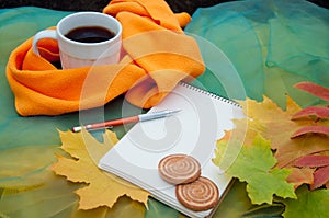 Autumn. Cup of tea, cookies, notepad, pencil and fallen leaves on green background