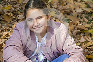 On an autumn day, a girl sits in the leaves in the park