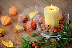 Autumn decoration with rose hips and burning candle in glass