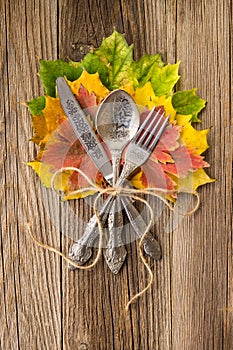 Autumn dinner place setting for Thanksgiving holiday with colorful maple leaves on rustic wooden boards