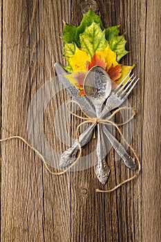 Autumn dinner place setting for Thanksgiving holiday with colorful maple leaves on rustic wooden boards