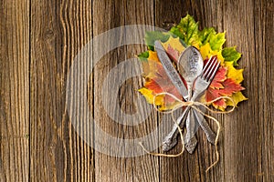 Autumn dinner place setting for Thanksgiving holiday with colorful maple leaves on rustic wooden boards
