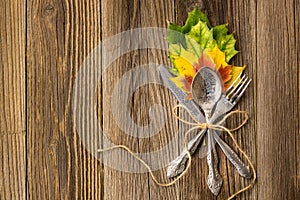 Autumn dinner place setting for Thanksgiving holiday with colorful maple leaves on rustic wooden boards