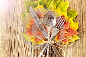 Autumn dinner place setting for Thanksgiving holiday with colorful maple leaves on rustic wooden boards