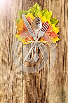 Autumn dinner place setting for Thanksgiving holiday with colorful maple leaves on rustic wooden boards