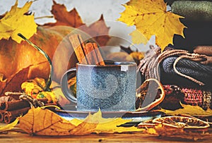 Autumn drink in blue cup on fall background with pumpkins, orange fallen leaves, autumn clothes, scarves on rustic wooden table,