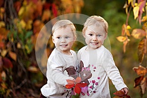 Autumn emotional portrait of little twin girls. Pretty little girls with red grape leaves in autumn park. Autumn activities for