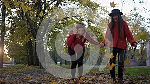 Autumn entertainments, smiling laughing young women have fun run holding hands and scatter yellow fallen leaves feet