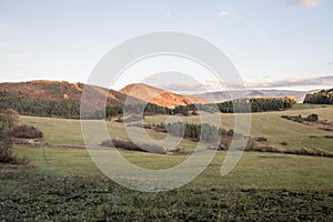 Autumn evening scenery with meadows, hills covered by colorful forest and blue sky with few clouds near Rajecke Teplice spa in