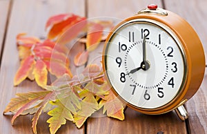 Autumn fall concept, alarm clock with red leaves on a wooden background