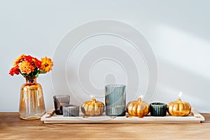 Autumn, fall cozy composition. Fresh dahlia flowers in vase and pumpkin shaped golden candles on the wooden tray with