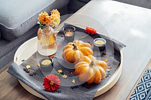 Autumn, fall cozy mood composition for hygge home decor. Small pumpkins, burning candles and fresh dahlia flowers on the tray with