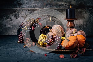 Autumn or fall harvest concept with lit candles, decorative pumpkins, corn, nuts, grapes and pinecones