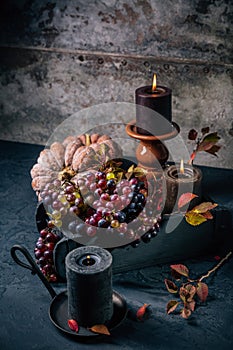 Autumn or fall harvest concept with lit candles, decorative pumpkins, corn, nuts, grapes and pinecones