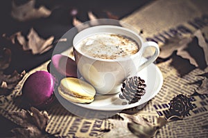 Autumn, fall leaves, hot steaming cup of cappuccino coffees, macaroons, cones on wooden table background.