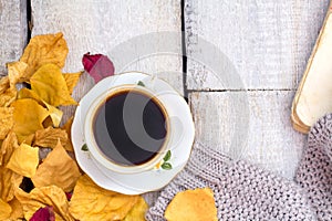 Autumn, fall leaves, hot steaming cup of coffee and a warm scarf on wooden table background..